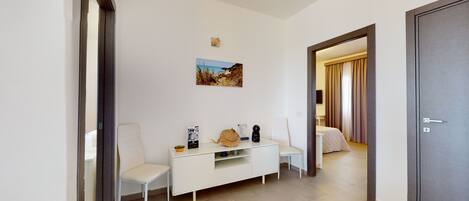 Habitación de hotel con una mesa consola blanca, una silla, una cama con cortinas, una puerta y una pequeña alfombra.