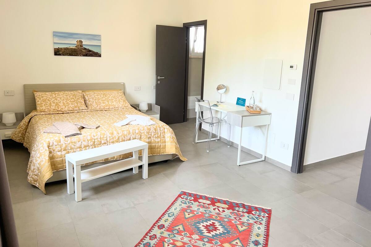 Un dormitorio con cama, mesita de noche, escritorio, silla y alfombra.