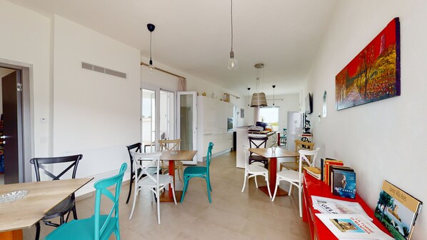 Una cocina moderna con armarios blancos, un comedor con mesa y sillas de madera, y una librería roja llena de libros.
