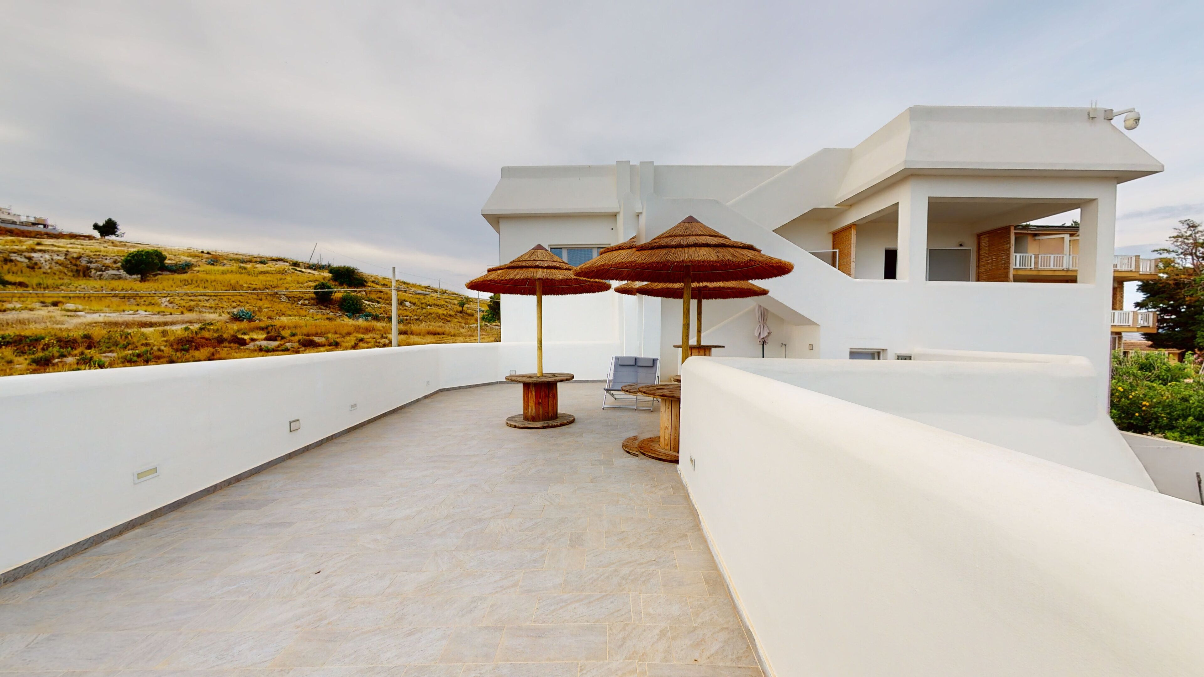 Un edificio moderno blanco con terraza plana, mobiliario exterior y sombrillas.