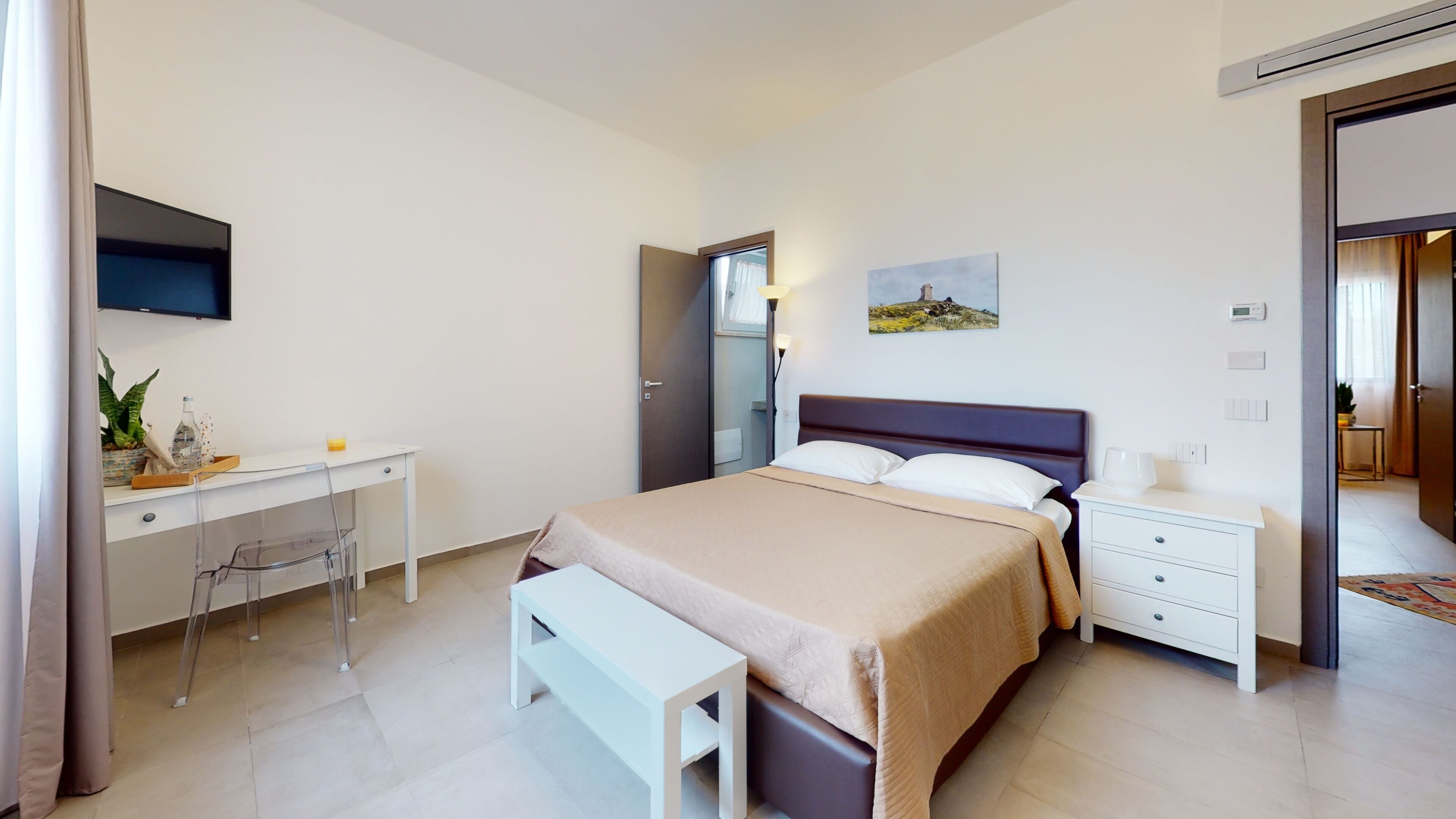 Una habitación de hotel moderna con cama, mesita de noche, escritorio, silla y un cuadro en la pared.