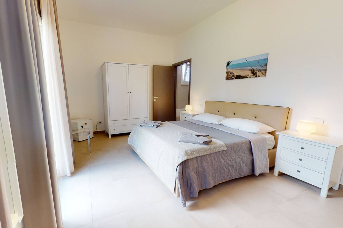 Un dormitorio con cama, mesitas de noche, armario y un cuadro en la pared.