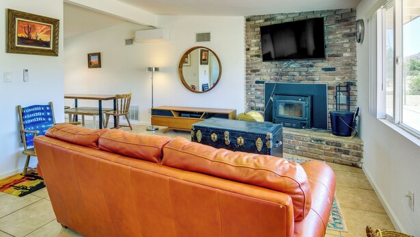A living room with a leather sofa, a fireplace, a TV mounted on a brick wall, and a dining area with a table and chairs.