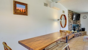 A dining area with a wooden table and chairs, a fireplace, a TV mounted on the wall, and a clock.