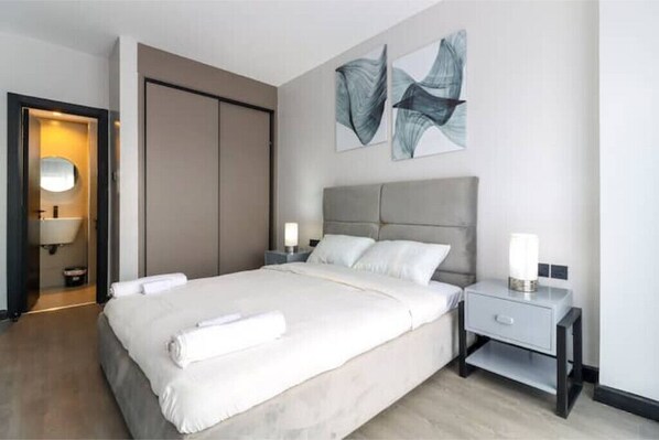 A modern hotel room with a large bed, two bedside tables, a wardrobe, and abstract wall art.