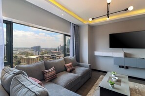 Ein modernes Wohnzimmer mit einem grauen Sofa, einem Couchtisch mit Pflanze und einem großen Fenster mit Blick auf die Stadt.
