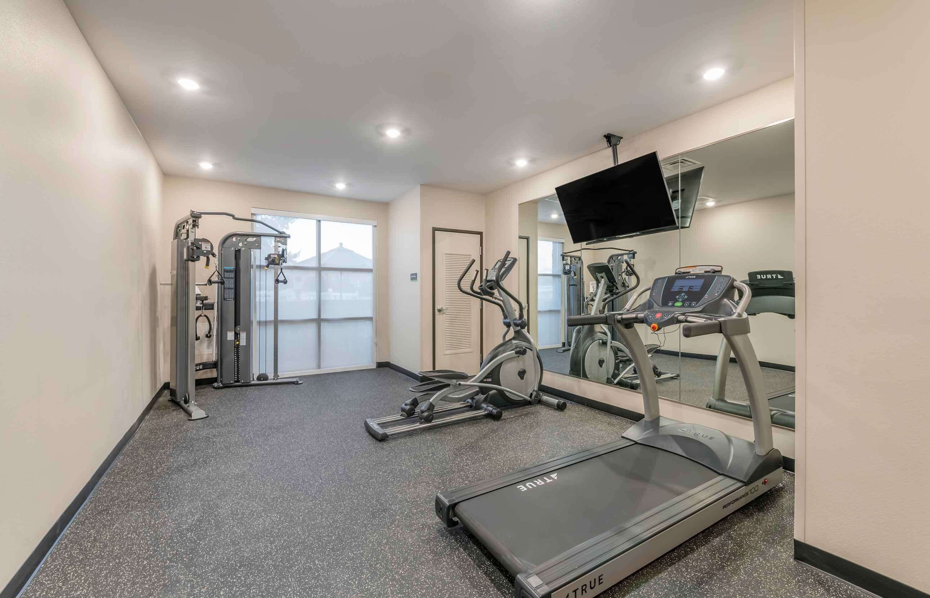 Un gimnasio con cinta de correr, elíptica y máquina de pesas.