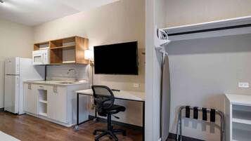 Una kitchenette compacta con microondas, refrigerador y pileta. Hay un escritorio con una silla y un televisor de pantalla plana montado en la pared.