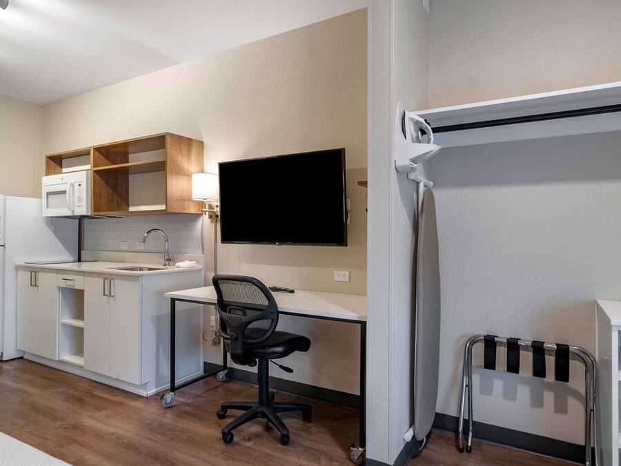 Una kitchenette compacta con microondas, refrigerador y pileta. Hay un escritorio con una silla y un televisor de pantalla plana montado en la pared.