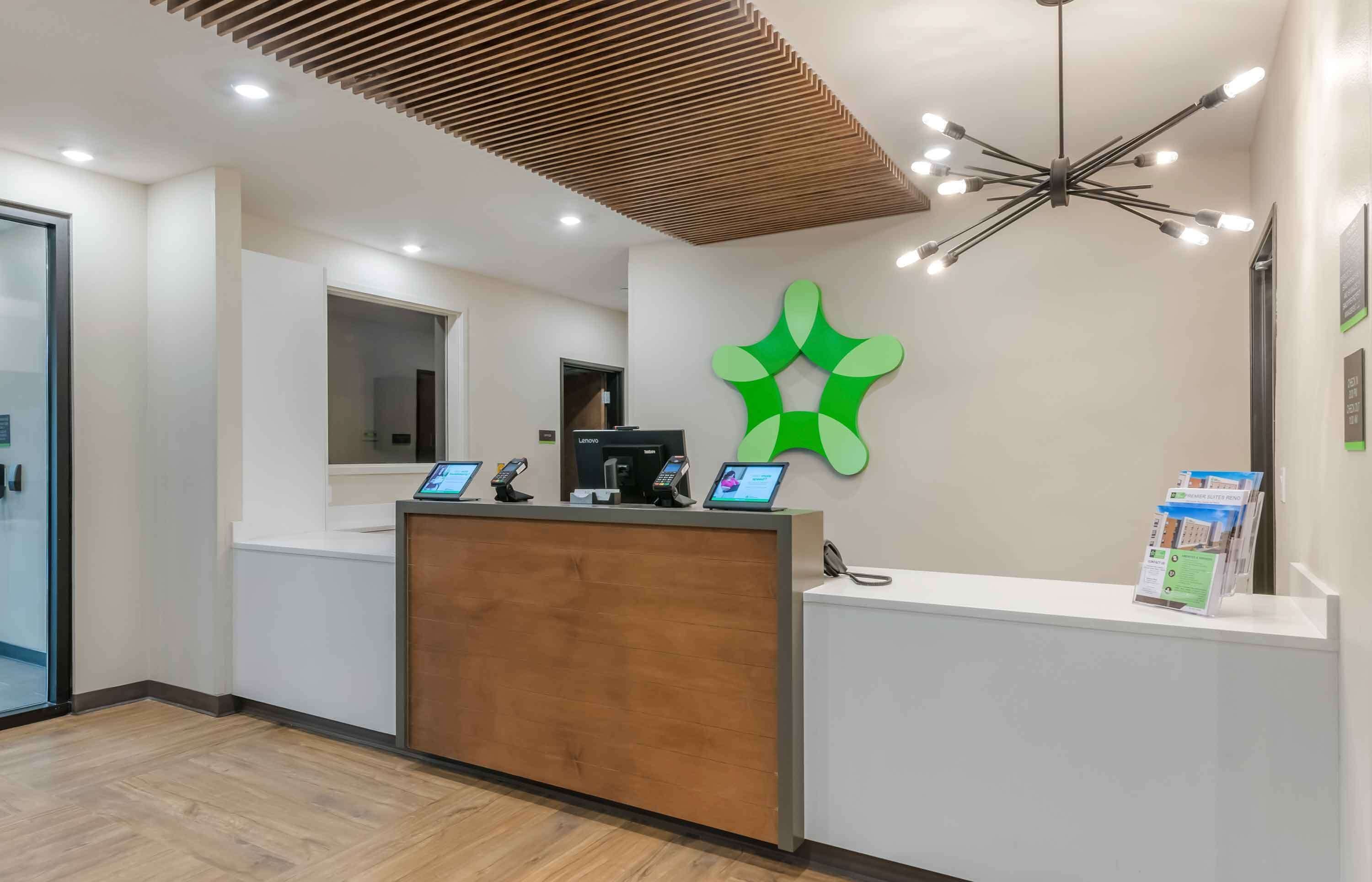 A reception area with a wooden reception desk, a green logo on the wall, and a ceiling light fixture.