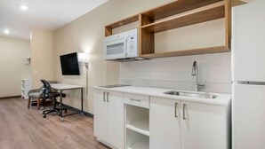 Une cuisine moderne avec des meubles blancs, un four à micro-ondes, un évier et une étagère en bois placée au-dessus du four à micro-ondes.