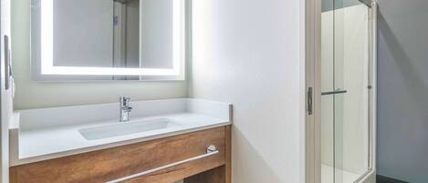A bathroom with a white sink, wooden vanity, and a glass shower enclosure.