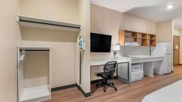 A hotel room with a bed, a desk with a chair, a TV, a microwave, and a refrigerator.