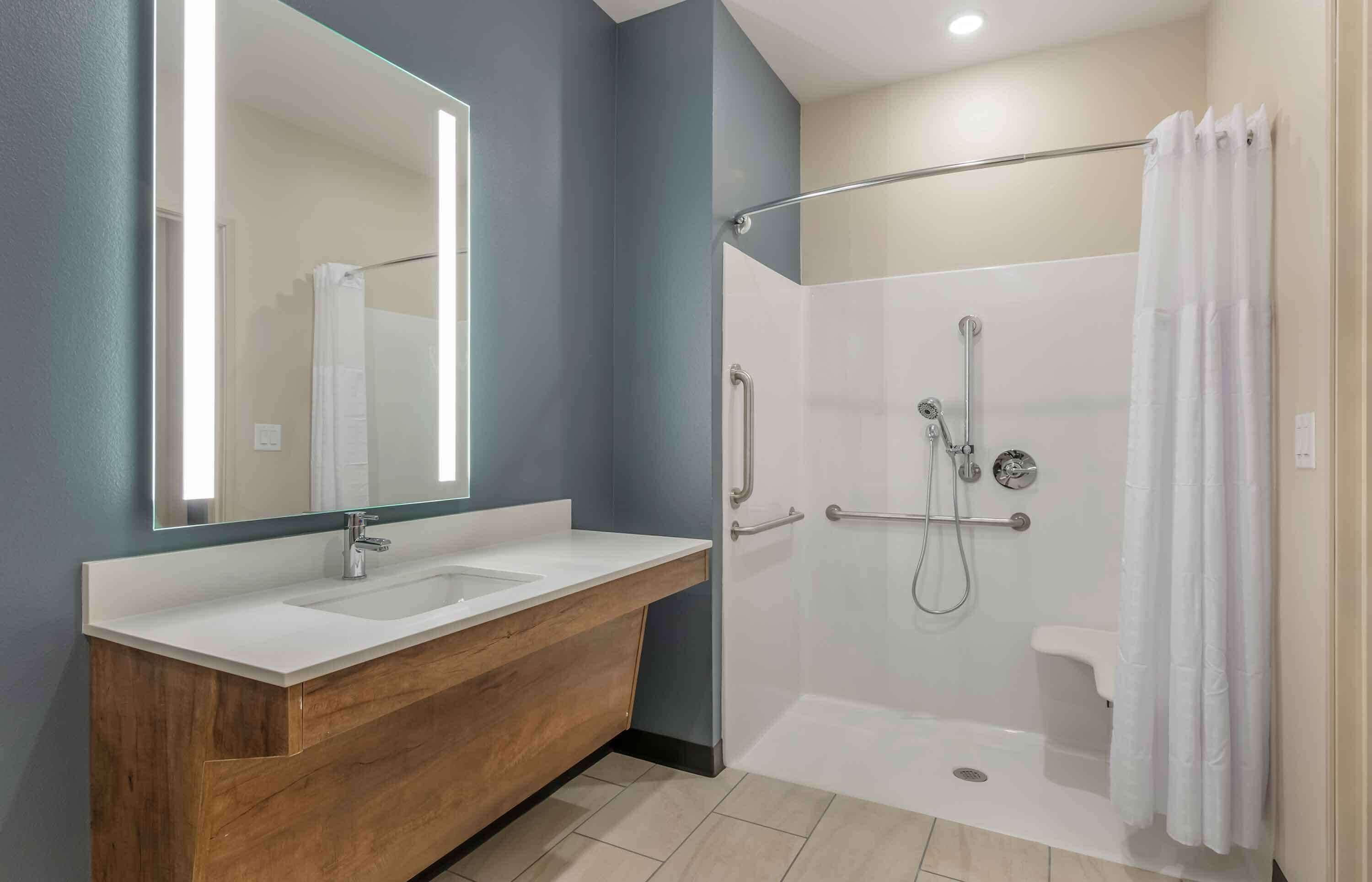 A modern bathroom with a wooden vanity, a large mirror, a shower with a glass door, and a white bathtub.