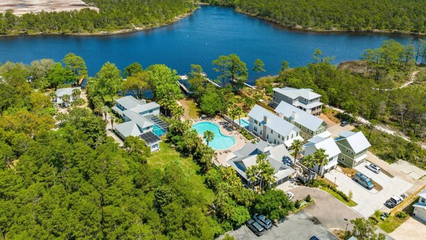 An aerial view of a resort with a large body of water, multiple buildings, and a swimming pool. - 30A Beach House - Pelican's Rest by PHG (Panama City Beach)