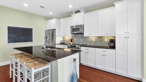 A modern kitchen with white cabinets, stainless steel appliances, and a large island with bar stools. - 30A Beach House - Pelican's Rest by PHG (Panama City Beach)