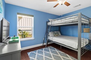 Habitación con literas, televisión, ventana con persianas, ventilador de techo y una alfombra azul.