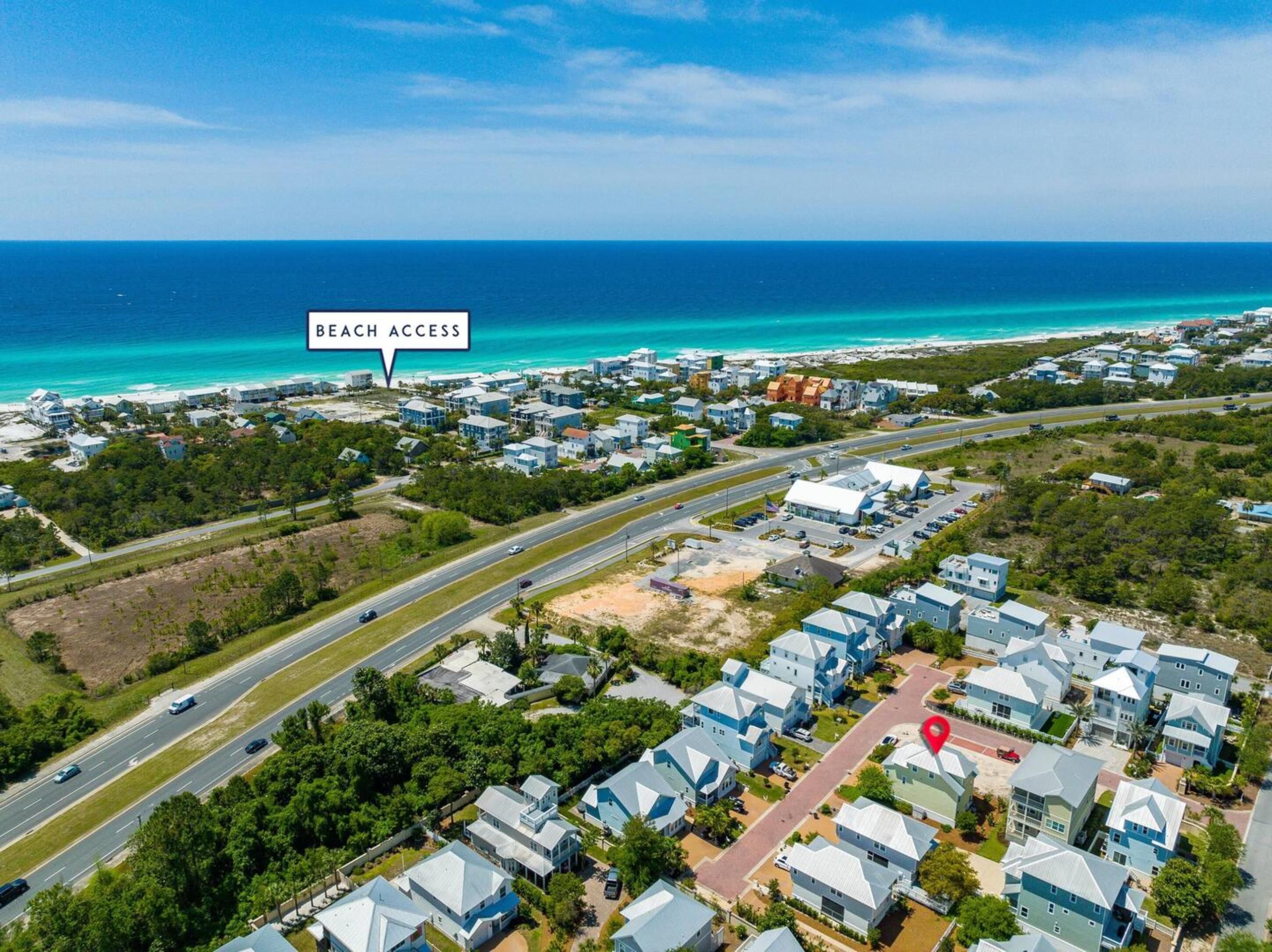 An aerial view of a coastal residential area with houses, roads, and a beach access point.