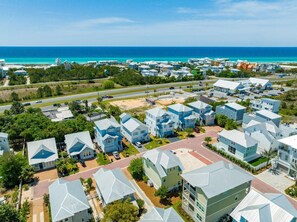 Un quartier résidentiel situé sur la côte, avec des maisons aux façades bleu clair et blanches, offrant une vue dégagée sur l’océan, et une route au premier plan.