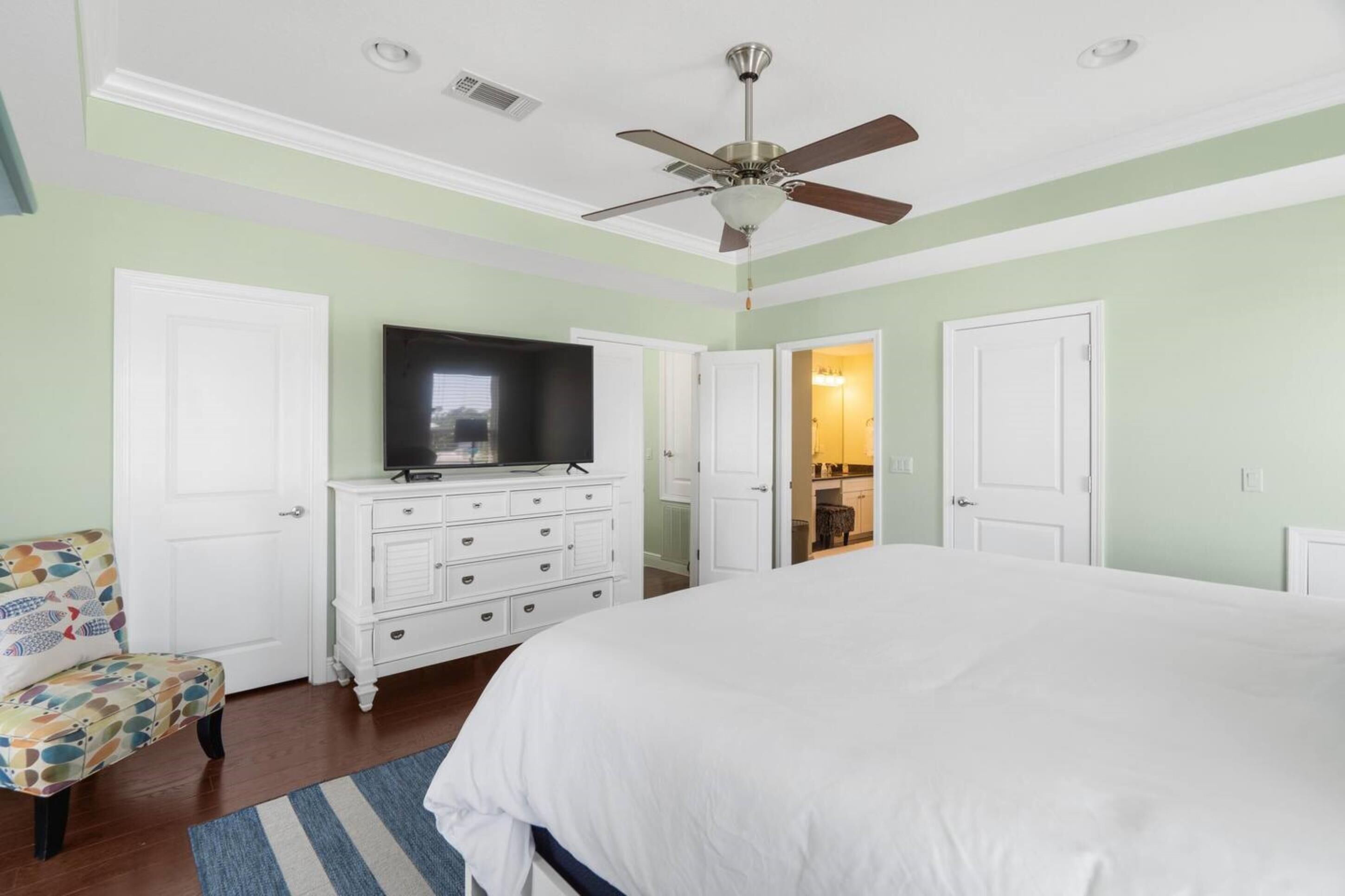 A bedroom with a bed, a dresser, a television, and a ceiling fan.