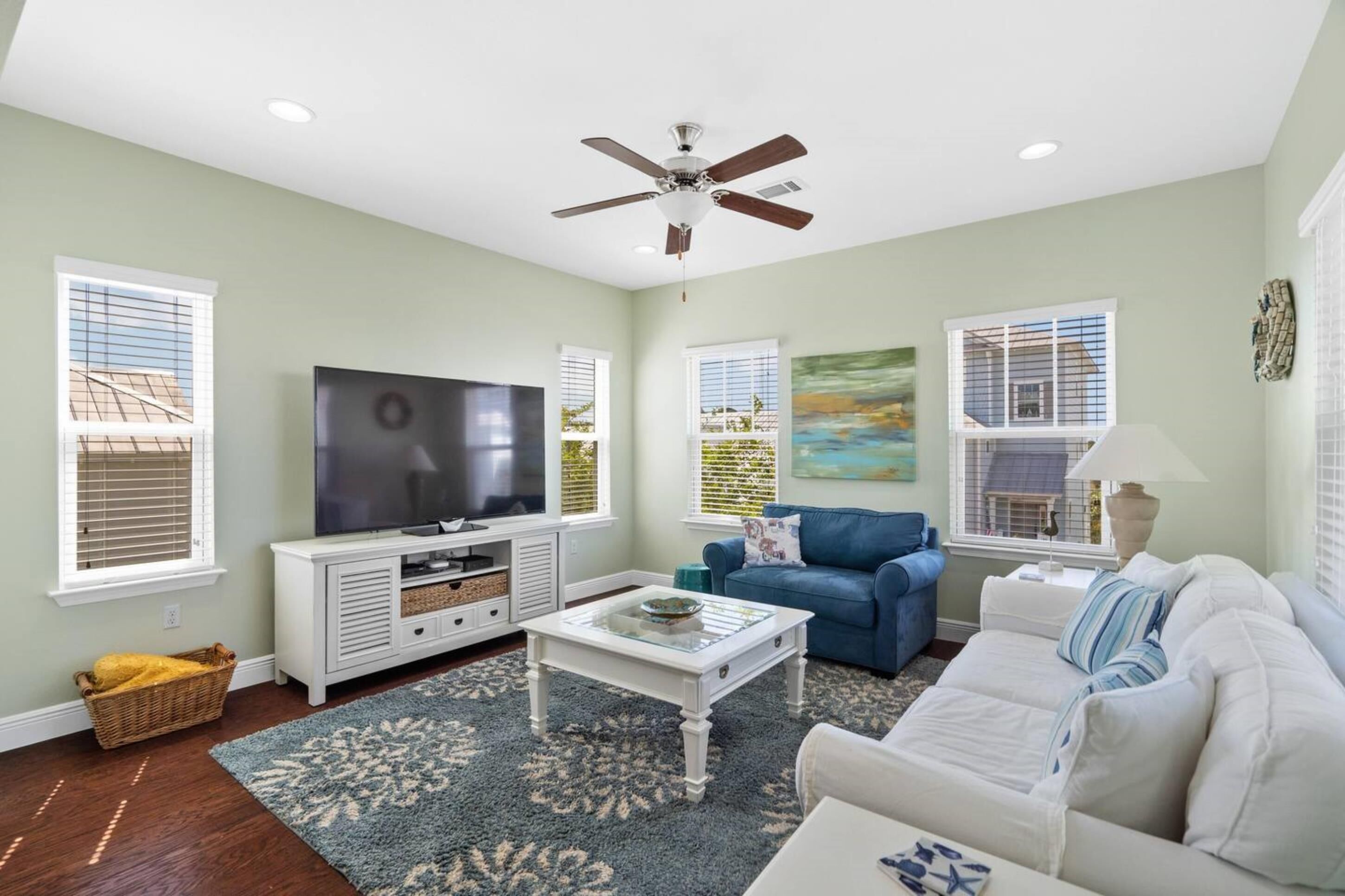 A living room with a TV, blue sofa, white couch, and a ceiling fan.