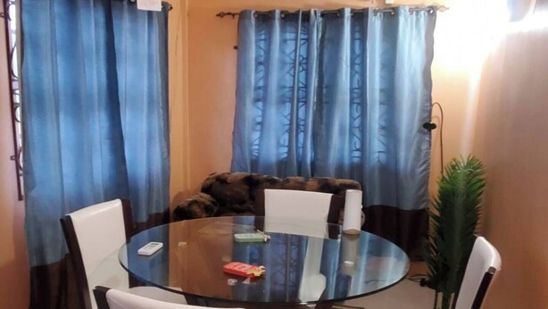 Uma sala de jantar com uma mesa redonda de vidro, rodeada por cadeiras, um ventilador de teto e cortinas azuis.