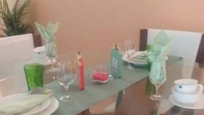 Uma mesa de jantar com cadeiras, tampo de vidro e diversos elementos de decoração, como pratos, copos e um vaso.