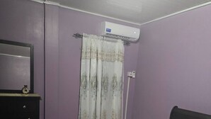Quarto com cama, cômoda, espelho, ar condicionado e cortina.