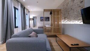 Een moderne woonkamer met een grijze bank, een houten bankje en een aan de muur bevestigde televisie.