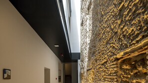 Een gang met aan de ene kant een structuurwand en aan de andere kant een egale wand, voorzien van inbouwverlichting.