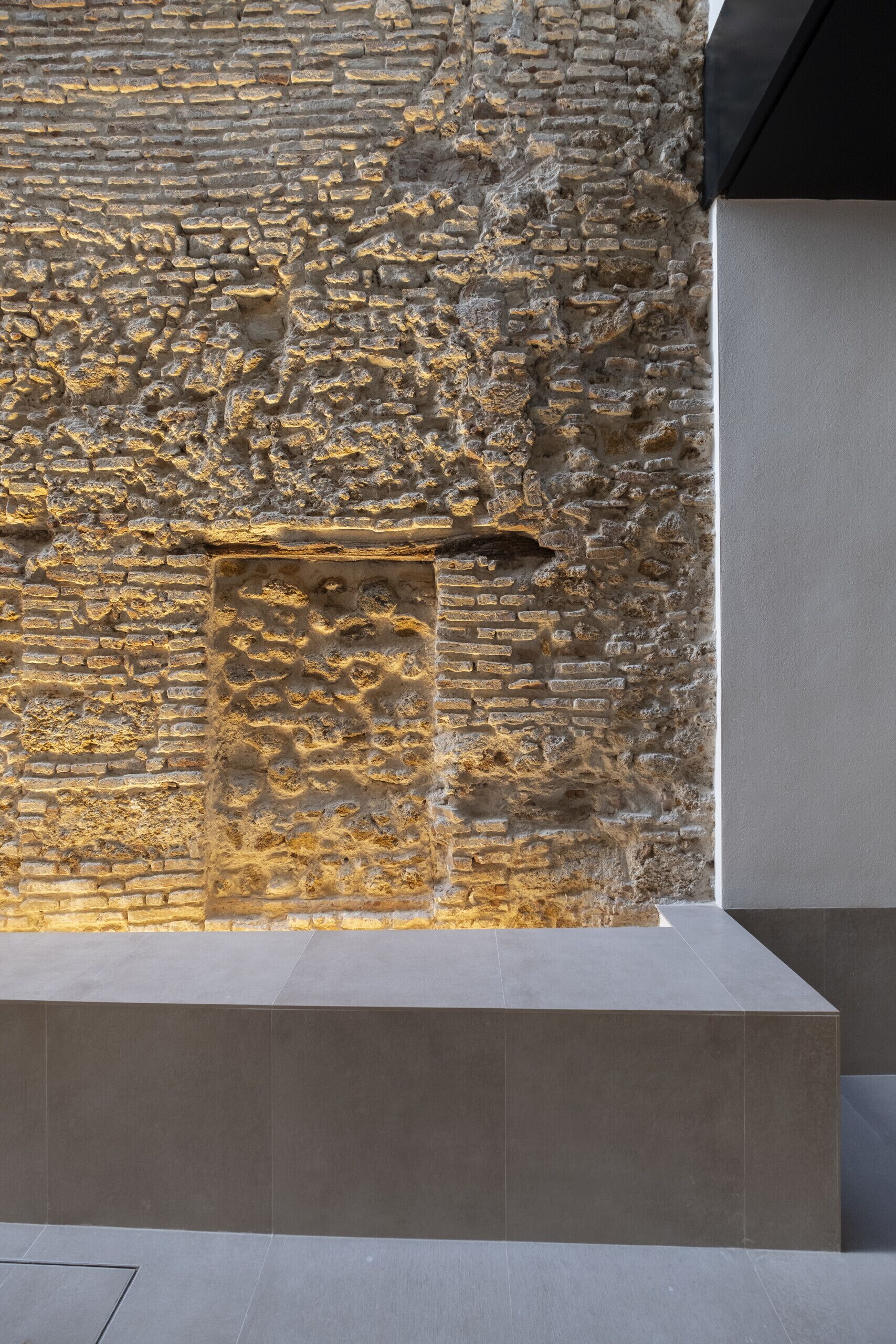 Pared de piedra con un panel hundido, suelo de baldosas modernas y techo plano.
