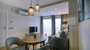 Un salon moderne comprenant un coin repas, des meubles recouverts d’un tissu gris, une table ronde en bois et un éclairage suspendu.