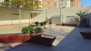Un espacio al aire libre con macetas que contienen pequeños árboles y arbustos, una estructura metálica y un edificio al fondo.