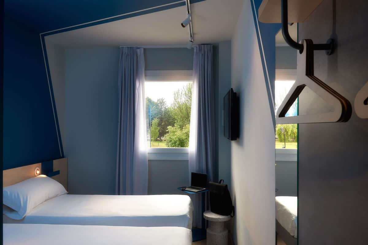 Una habitación de hotel con cama, escritorio, silla, televisor y ventana con cortinas.