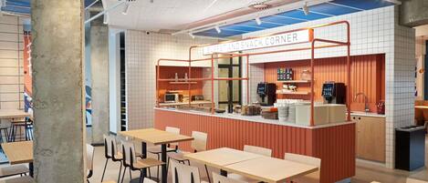 Una cafetería con mostrador que indica 'Coffee and Snack Corner', mesas, sillas y una zona de cocina.