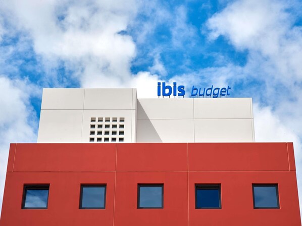 A building with 'ibis budget' signage, multiple windows, and a clear sky in the background.