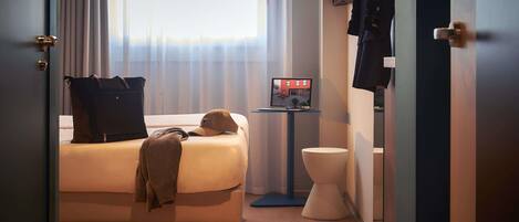 Una habitación de hotel con cama, maleta, televisor y un inodoro.