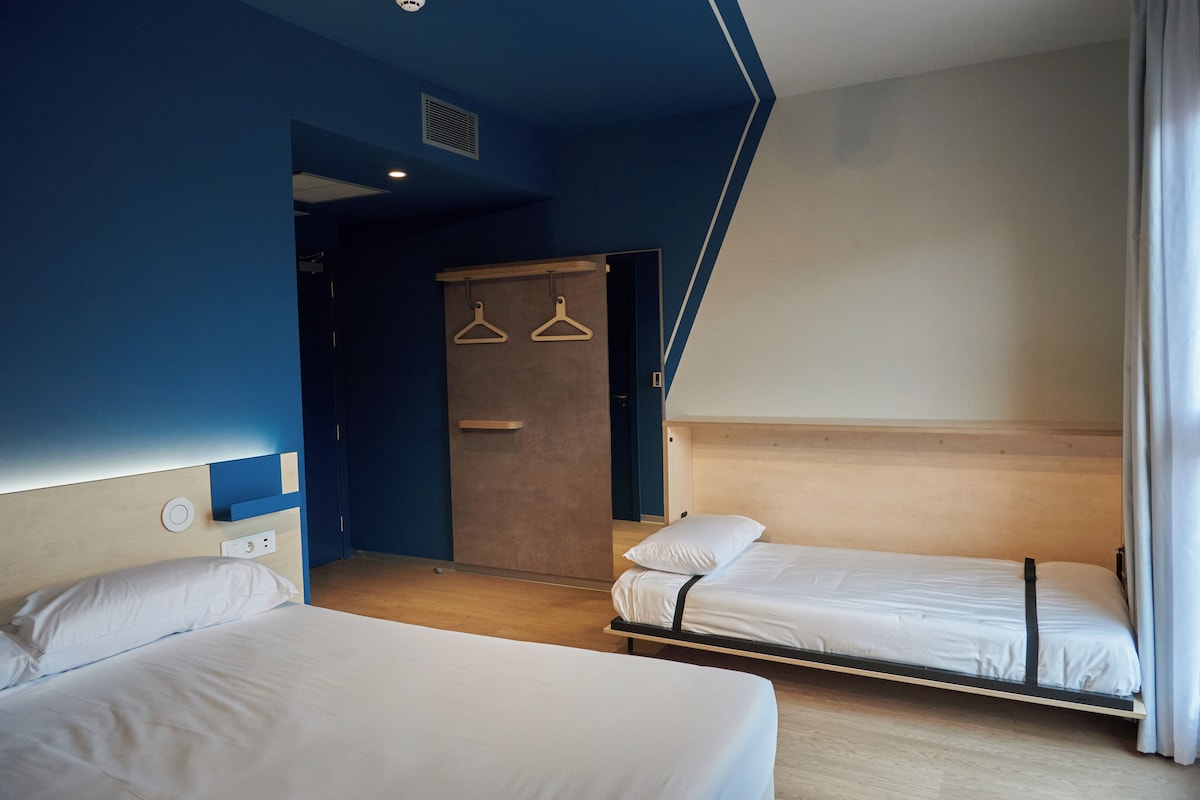 Une chambre d’hôtel avec deux lits simples, une tête de lit en bois, une armoire et un porte-vêtements.