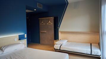 A hotel room with two single beds, a wooden headboard, a wardrobe, and a hanging clothes rack.