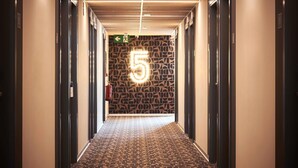 A hallway with a patterned carpet, a wall with a geometric design, and an illuminated number '5' sign.