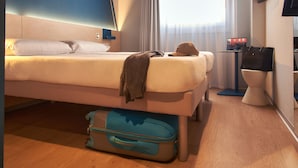Una habitación de hotel con una cama, una maleta, un escritorio con una computadora y una ventana con cortinas.