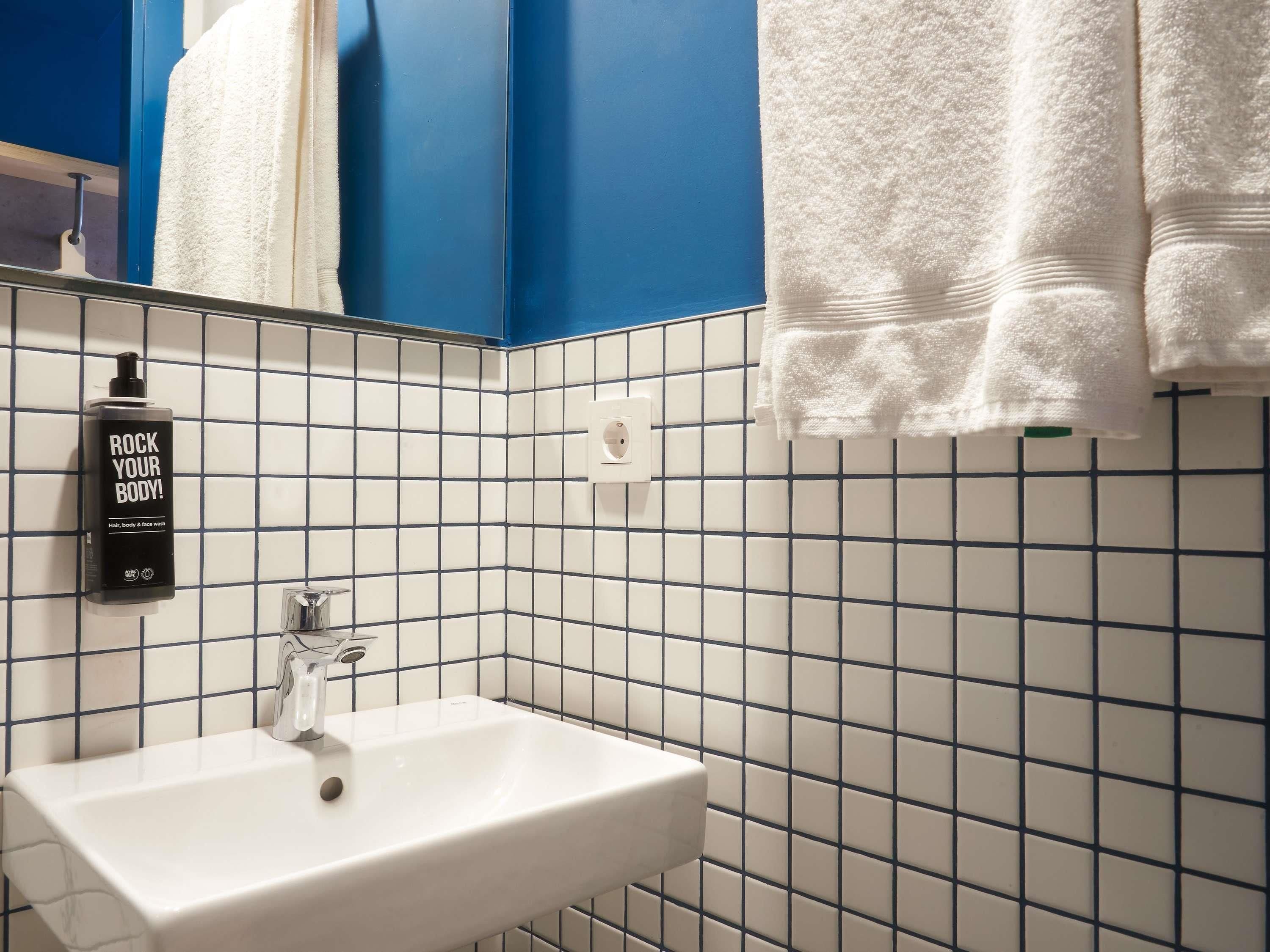 Ein Badezimmer mit einem weißen Waschbecken, einem Spiegel, einem Handtuchhalter mit weißen Handtüchern und einer Flasche Duschgel.