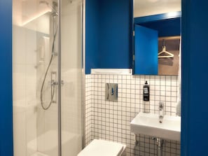 A modern bathroom with a glass-enclosed shower, a white sink with a mirror, and a blue accent wall. - Ibis Budget Vitoria Gasteiz (Vitoria-Gasteiz)