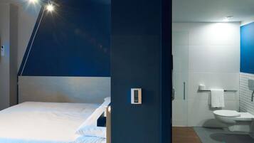 Una habitación de hotel moderna con una cama, un panel de control y vistas al baño.