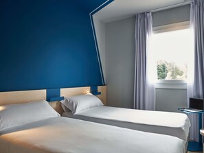 Une chambre d’hôtel avec deux lits, un bureau avec un ordinateur portable et une fenêtre avec des rideaux.