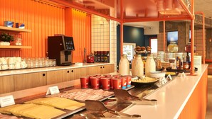 Zona de bufé con diversos alimentos, utensilios, una máquina de café y una barra con tazas y platos.