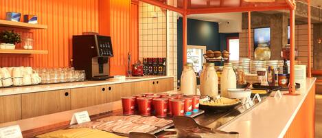 A buffet area with various food items and utensils, a coffee machine, and a counter with cups and plates.