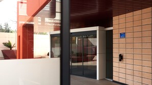 Una entrada moderna de edificio con puerta de vidrio, toldo rojo y suelo de baldosas.