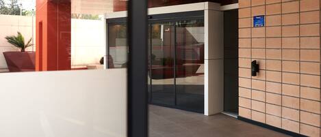Una entrada moderna de edificio con puerta de vidrio, toldo rojo y suelo de baldosas.