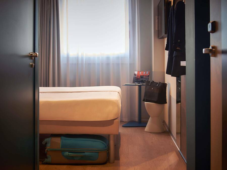 A hotel room with a bed, a suitcase, a laptop on a small table, and a toilet.